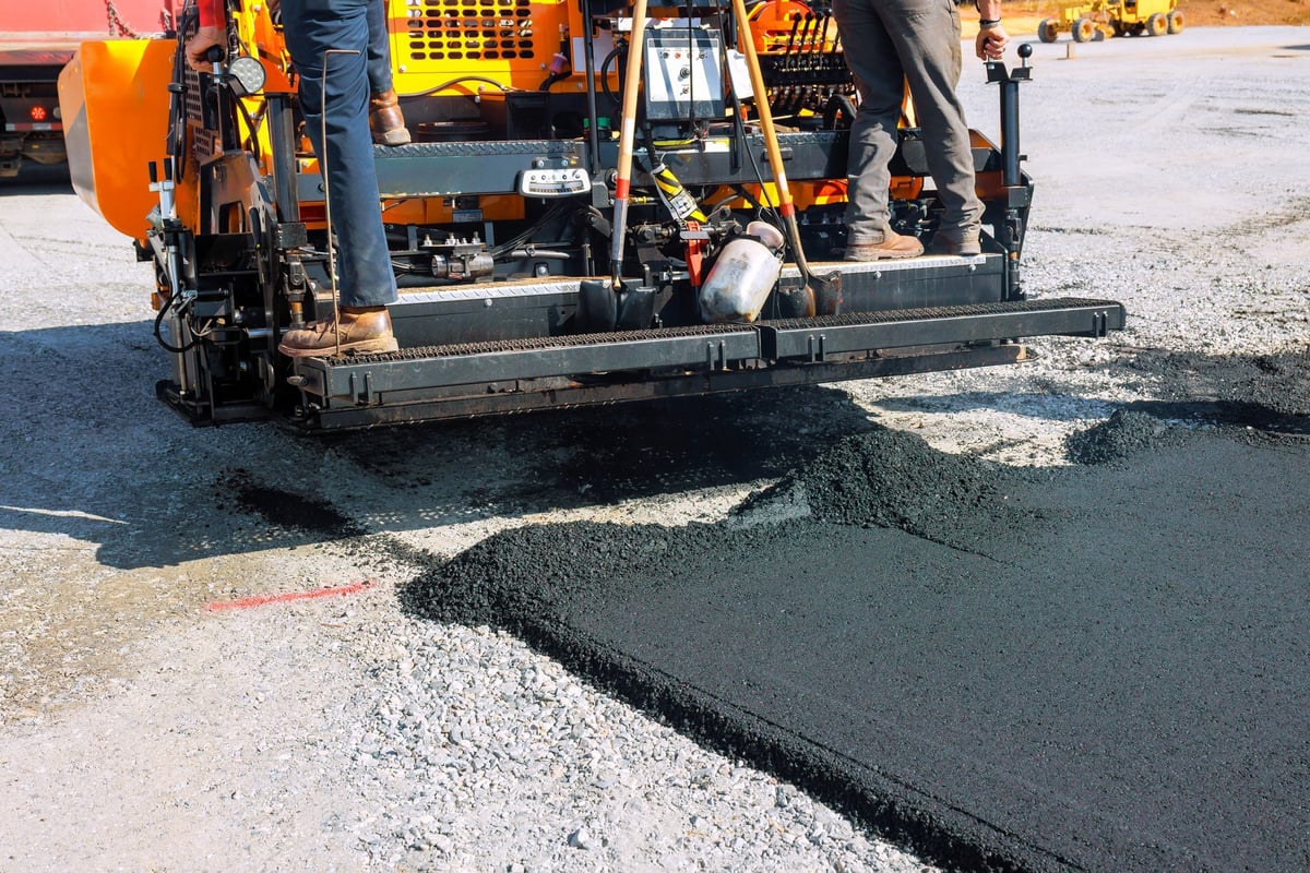 Workers operating a paving machine laying new asphalt on a public road construction site